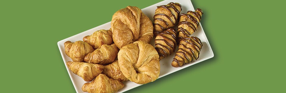 White, rectangular platter with crois-sants, mini croissants and croissants with choco-late drizzle. Platter is on a green background.