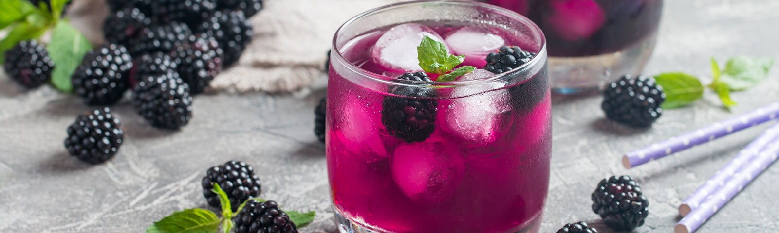 Magenta colored drink with ice cubes and blackberries