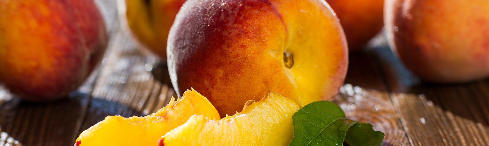 Multiple peaches on wooden table with green leaves