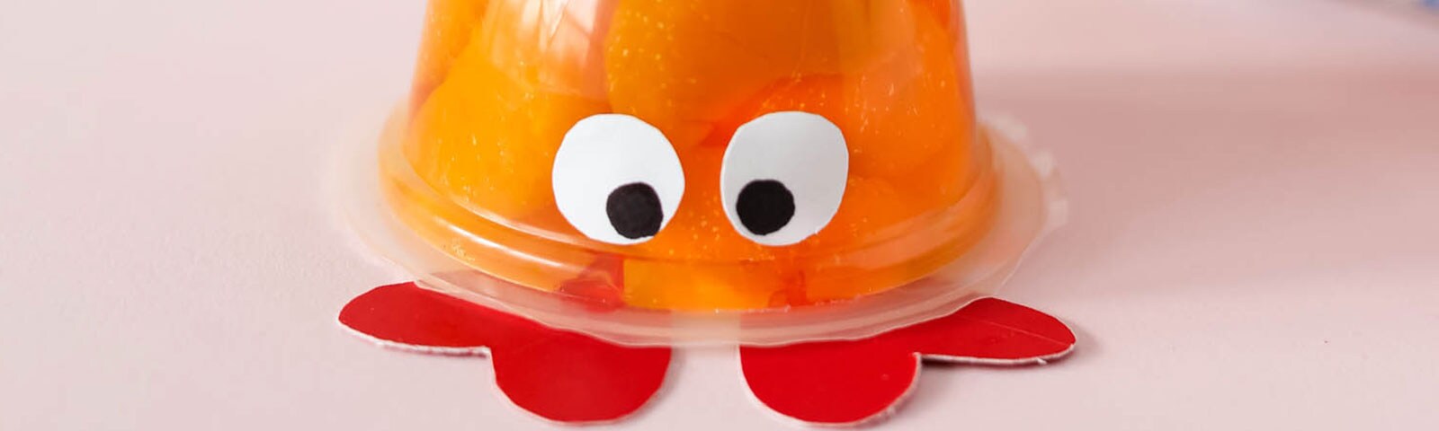 An upside down fruit cup with eyes made out of paper and hearts for feet