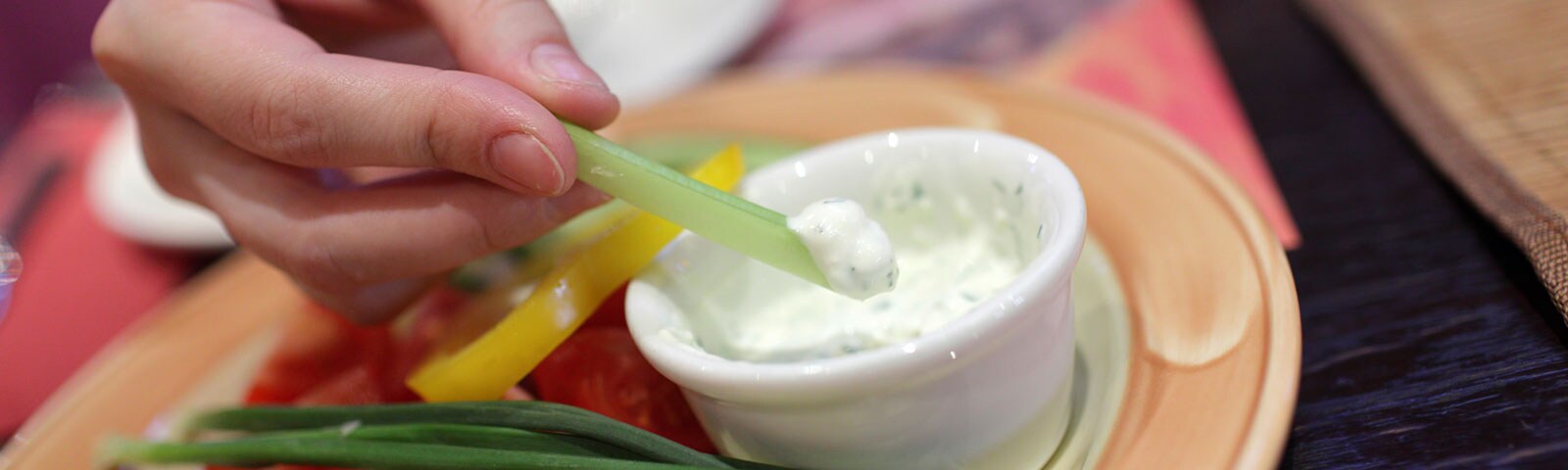 A pair of hands dipping vegetables into a cup of dip A pair of hands dipping vegetables into a cup of dip