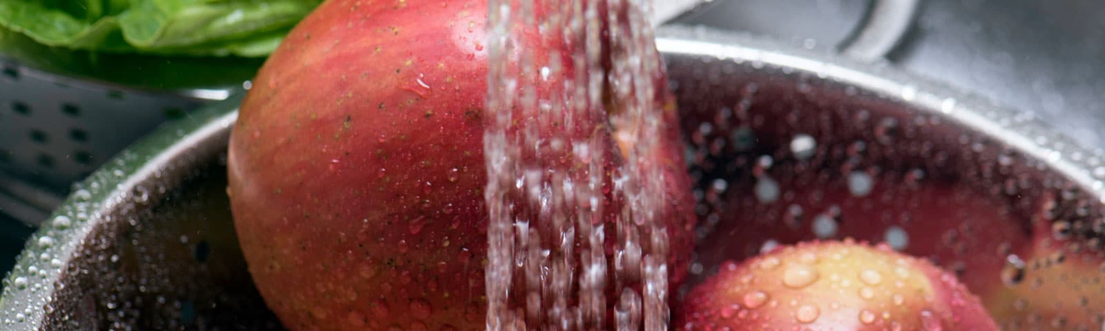 Washing red apples in a metal bowl with running water