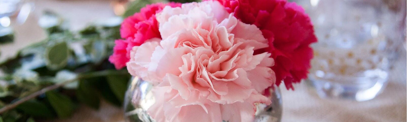 Pink and red carnations sitting in a large bulbous vase atop a table 