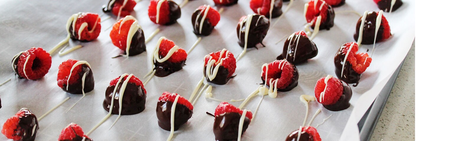 Rows of chocolate-dipped raspberries with a white chocolate drizzle on parchment paper Rows of chocolate-dipped raspberries with a white chocolate drizzle on parchment paper