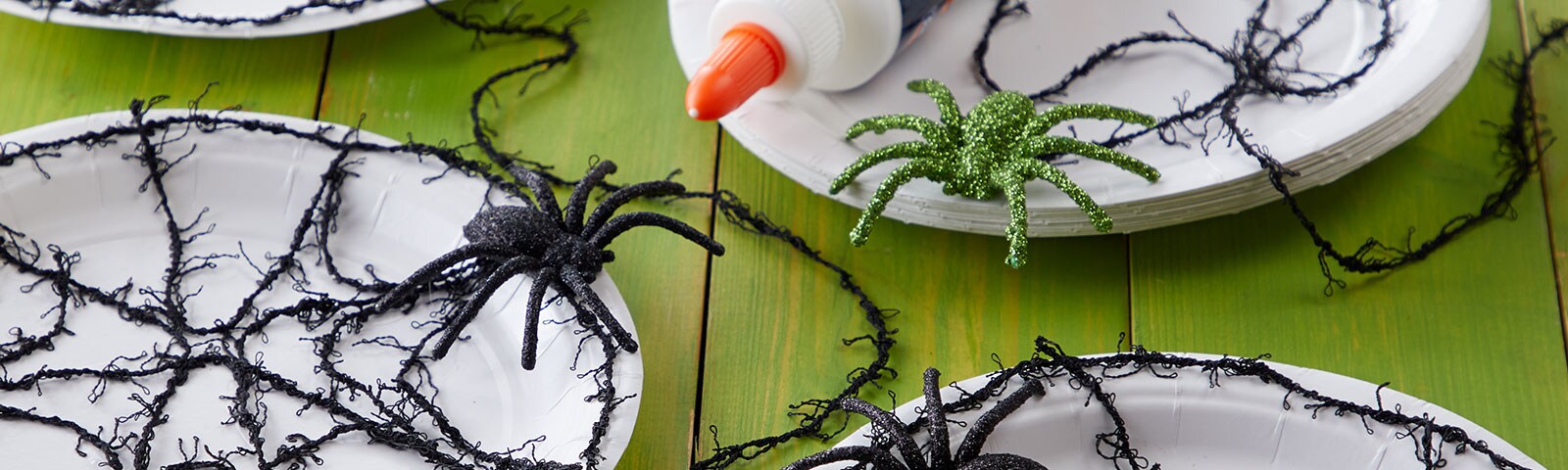 White paper plates with black yarn spiderwebs and black plastic spiders on top White paper plates with black yarn spiderwebs and black plastic spiders on top