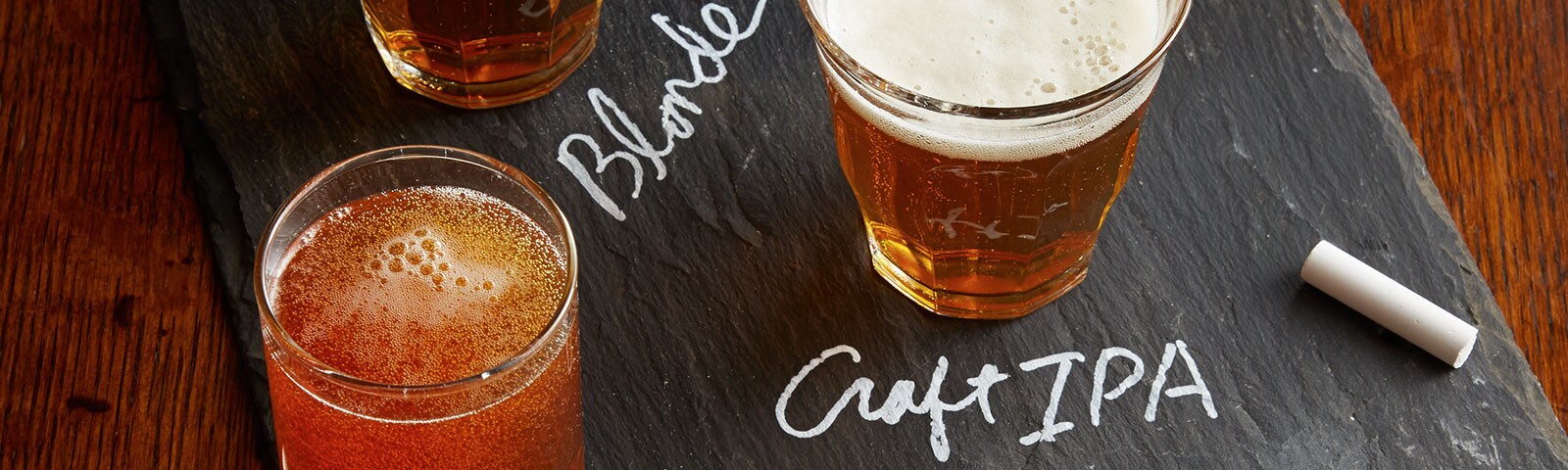 Craft beer flight with a row of glasses on a chalkboard and the words "Blonde" and "Craft IPA" written out in chalk Craft beer flight with a row of glasses on a chalkboard and the words "Blonde" and "Craft IPA" written out in chalk
