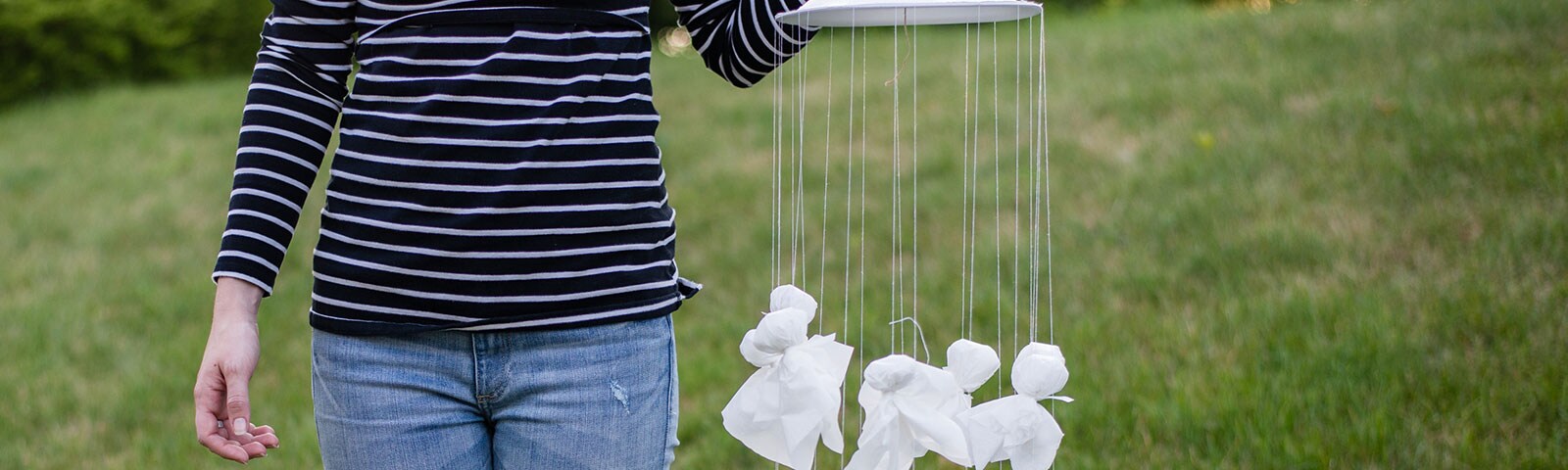 Woman holding a homemade mobile with multiple tissue ghosts hanging from a plate