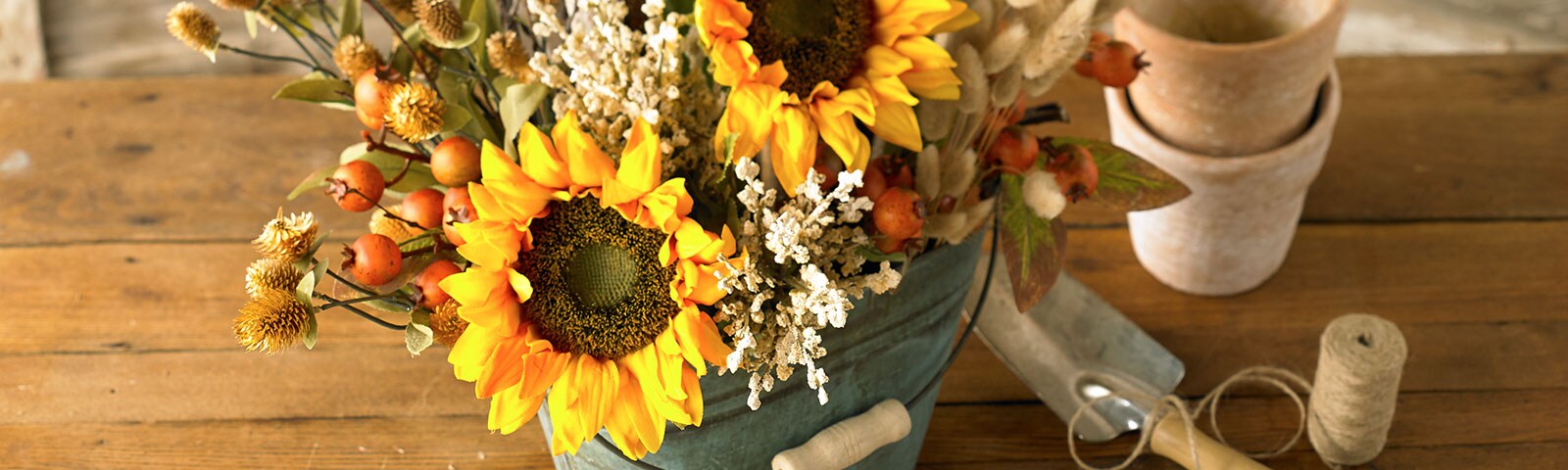 Sitting on a rustic wooden table a metal bucket is filled with sunflowers and other fall blooms. Sitting on a rustic wooden table a metal bucket is filled with sunflowers and other fall blooms.