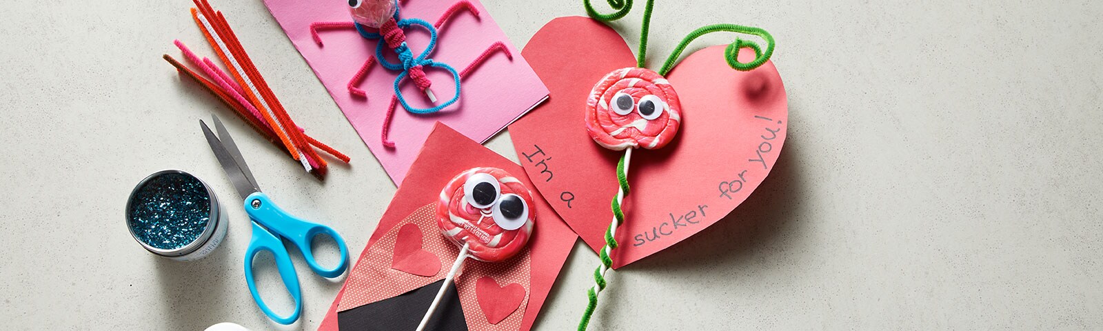 Table scattered with craft supplies and three homemade valentine's cards fashioned as bugs with candy as the main component