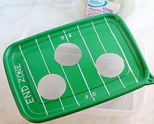 Decorated green rectangle container lid with 50-yard line and end zones drawn in white marker