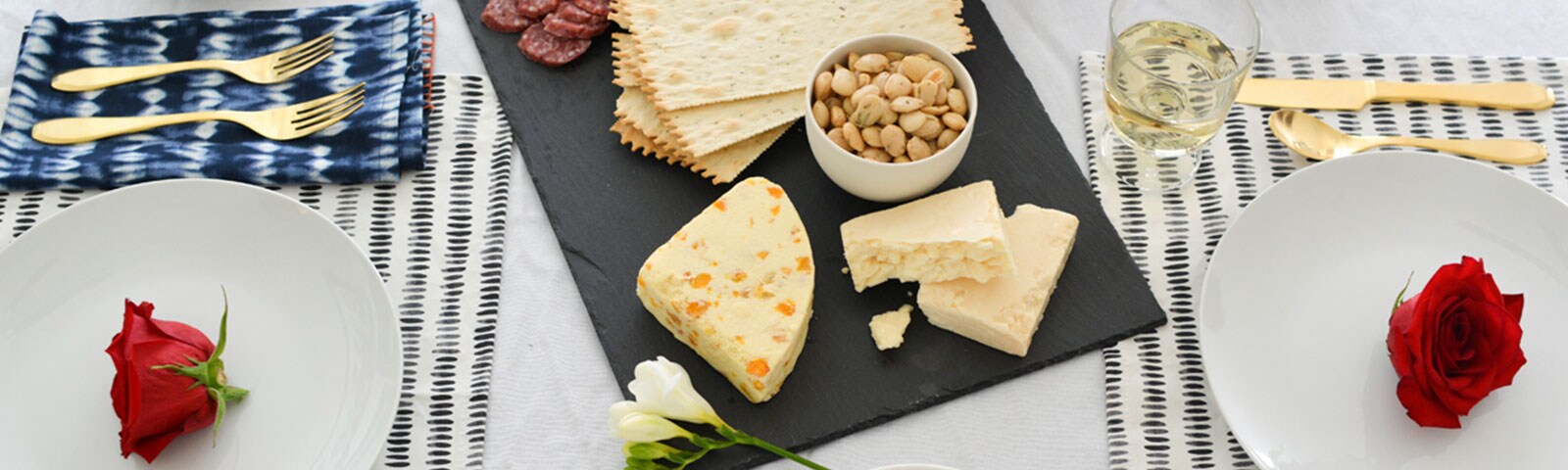 A table on top of which lays a charcuterie board, linen napkins with golden forks, and round white plates with a rose flower in the center A table on top of which lays a charcuterie board, linen napkins with golden forks, and round white plates with a rose flower in the center