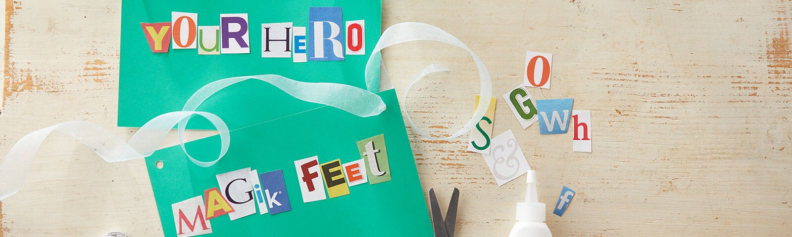 Two green cards on a wooden background, one says YOUR HERO using magazine clippings and the other say MAGIK FEET 