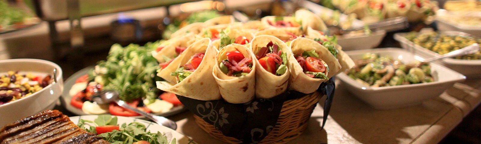 a bountiful feast of wraps, greens and pasta salads sit on a long countertop a bountiful feast of wraps, greens and pasta salads sit on a long countertop
