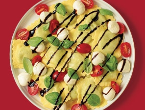 Cooked ravioli with tomatoes, mozza-rella and basil and balsamic glaze or dressing.