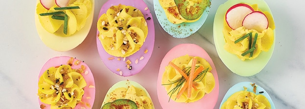 Assorted pastel deviled eggs with a variety of different toppings