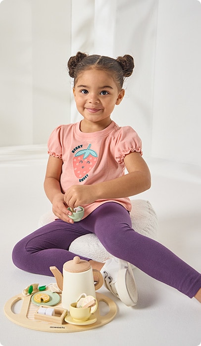 Young girl playing with a tea cup while wearing featured shirt with a strawberry on it