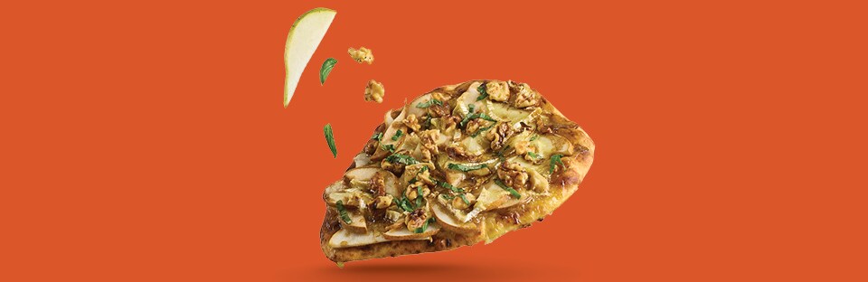 A Pear and Brie Naan floating on an orange background, with pieces of walnuts, pears and julienned basil floating on an orange background