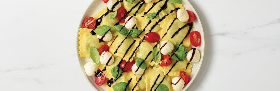 Ravioli with fresh tomatoes, mozzarella, and basil, drizzled with balsamic glaze