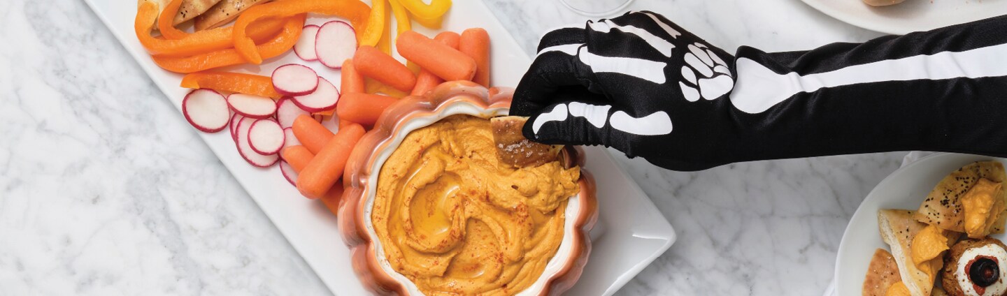 hand dipping Smoky Pumpkin Hummus and Pita Chips on platter with vegetables