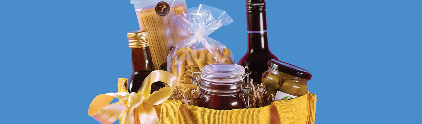 Arrangement of specialty olive oils, premium pasta, olives and a favorite wine in a reusable tote.