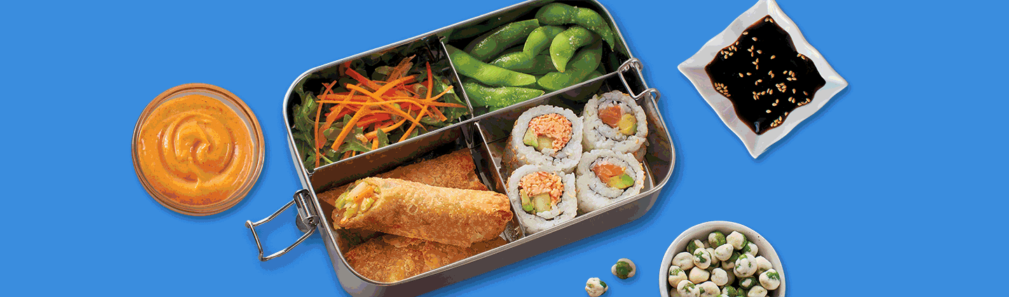 Bento Box filled with Edamame, Ginger Salad, Egg Rolls and Sushi. Side dishes of spicy